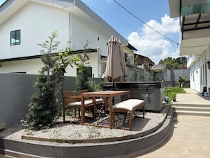 A patio area with a wooden table and chairs, surrounded by gravel and plants. - Villa with Office, Gym, Jacuzzi & Dryer near CIQ (Johor Bahru)