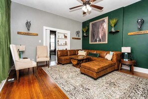A living room with a sectional sofa, a chair, a coffee table, a patterned rug, a ceiling fan, and decorative wall art. - Louisville Lore | Hot Tub • NuLu • Walk Everywhere (Louisville)