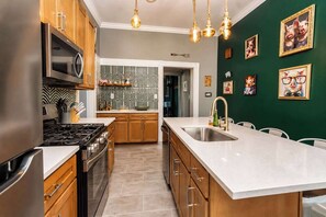 A modern kitchen with wooden cabinets, a stainless steel refrigerator, a gas stove, and a large island with a sink. - Louisville Lore | Hot Tub • NuLu • Walk Everywhere (Louisville)