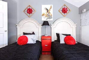Een hotelkamer met twee bedden, een rode kapstok en kunst aan de muur.