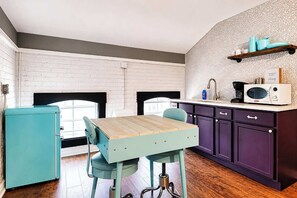 Eine kleine Küche mit einem Holztisch, blaugrünen Stühlen und violetten Schränken.