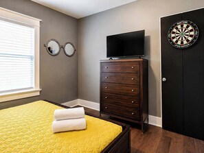 Une chambre à coucher avec un lit, une commode, un téléviseur et un jeu de fléchettes.