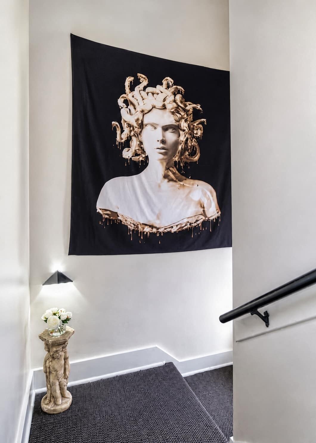 Una scala con una tessitura bianco e nero, un piccolo vaso con fiori e un lampadario a parete.