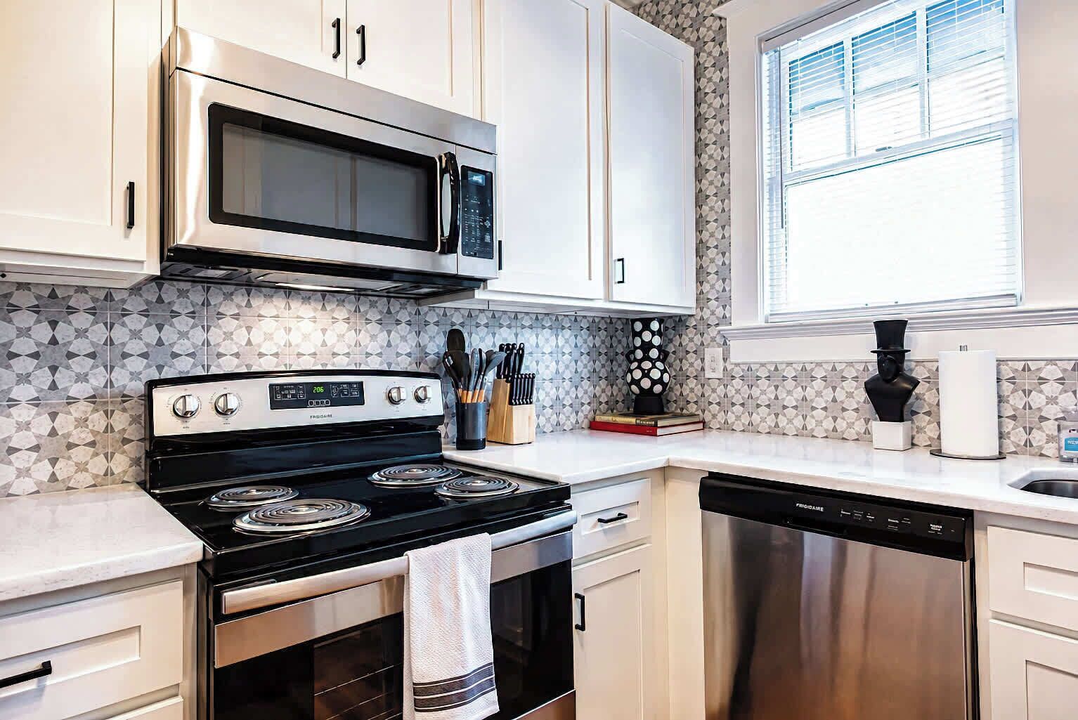 A kitchen with white cabinets, a stainless steel microwave, a stove, and a dishwasher.