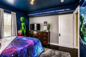 A bedroom with a bed, dresser, and a wall with a space-themed mural. - The Wild Side Retreat | Hot Tub • Walk Everywhere! (Louisville)