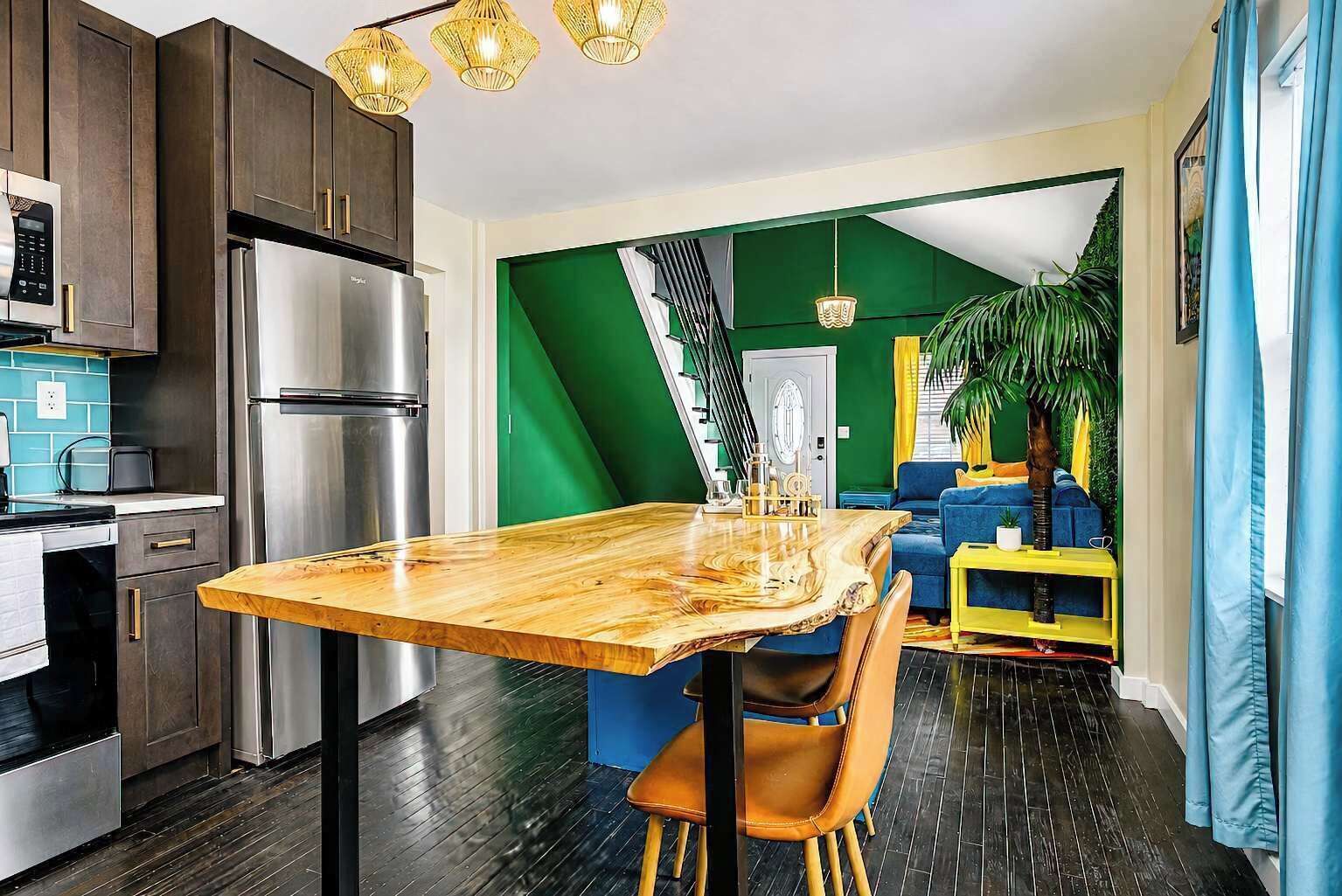 Une cuisine moderne avec une table à manger en bois, des appareils électroménagers en acier inoxydable et un mur d’accent vert.