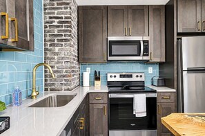 A modern kitchen with a stone accent wall, stainless steel appliances, and dark cabinetry. - The Wild Side Retreat | Hot Tub • Walk Everywhere! (Louisville)