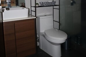 Een moderne badkamer met een wit toilet, een houten wastafelmeubel en een douchecabine van glas.