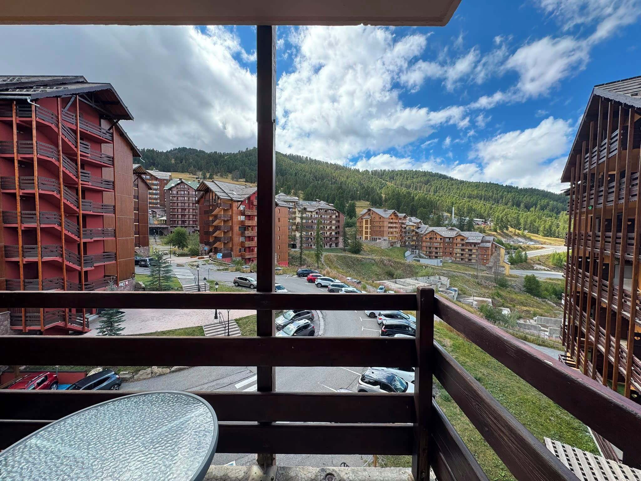 A balcony with a view of a mountain, a parking lot, and several multi-story buildings.