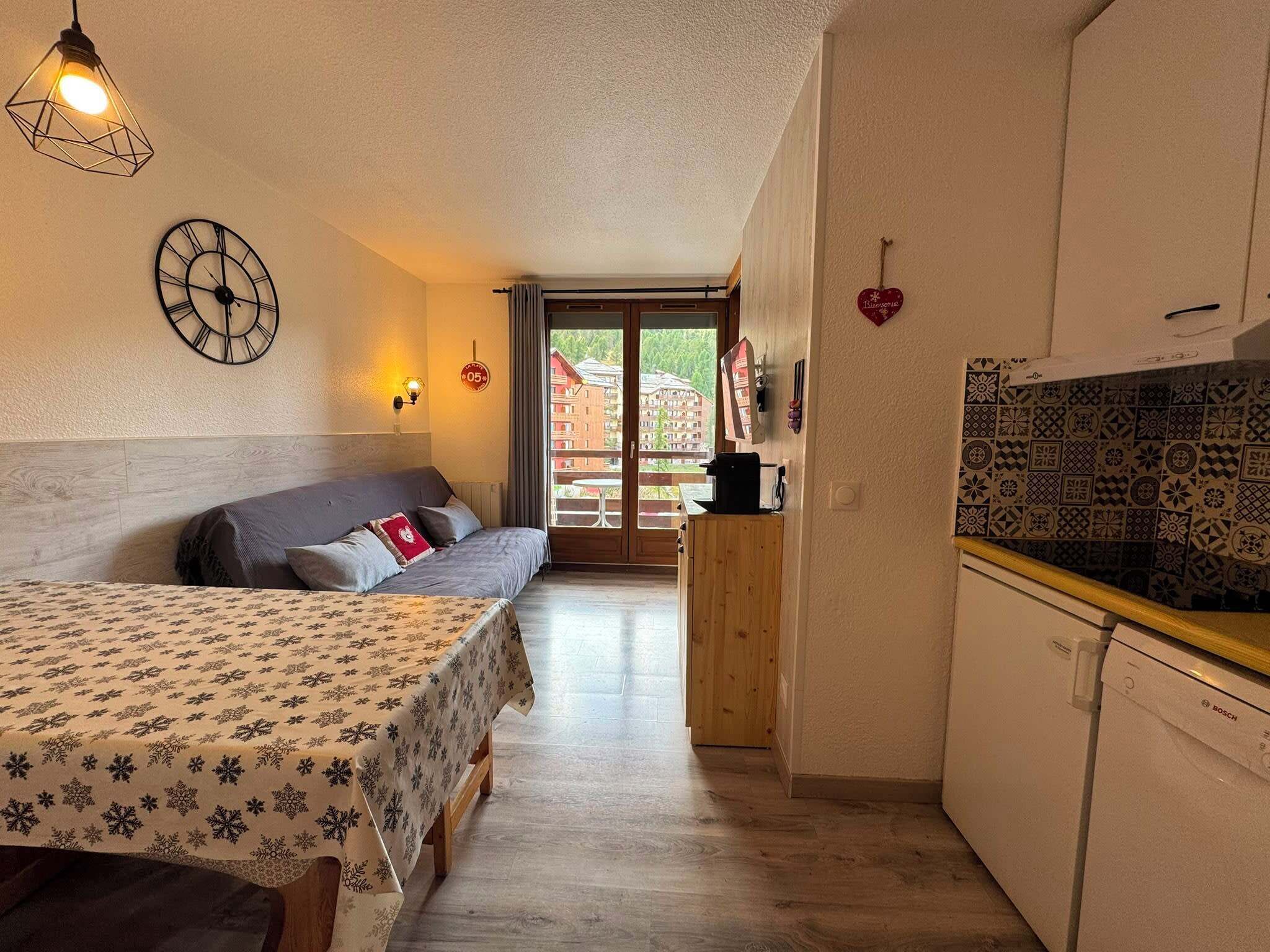 Une chambre d’hôtel compacte comprenant un lit, une petite kitchenette, une horloge murale et une vue sur l’extérieur.