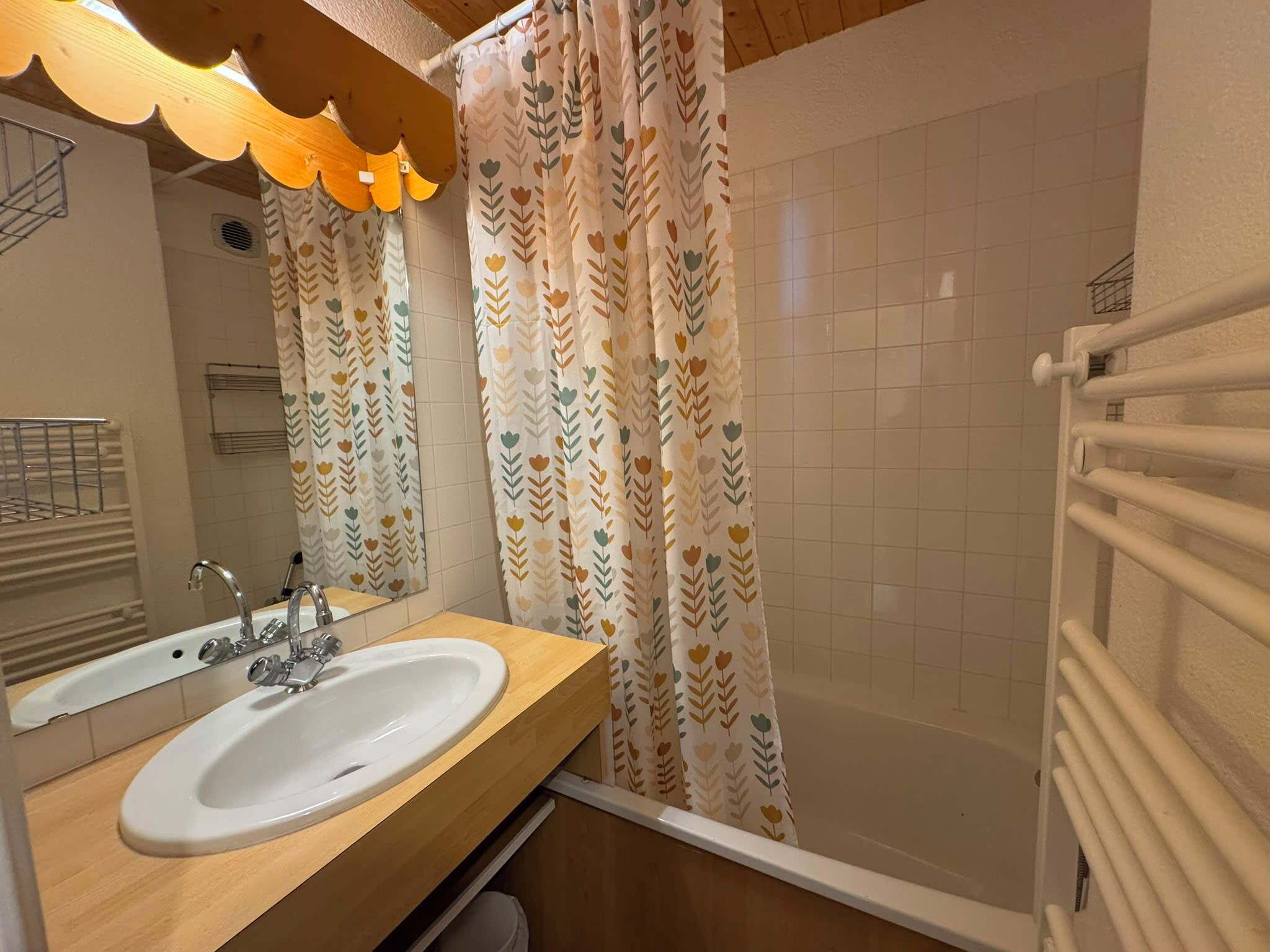 A bathroom with a white sink, a mirror, a shower with a patterned curtain, and a towel rack.