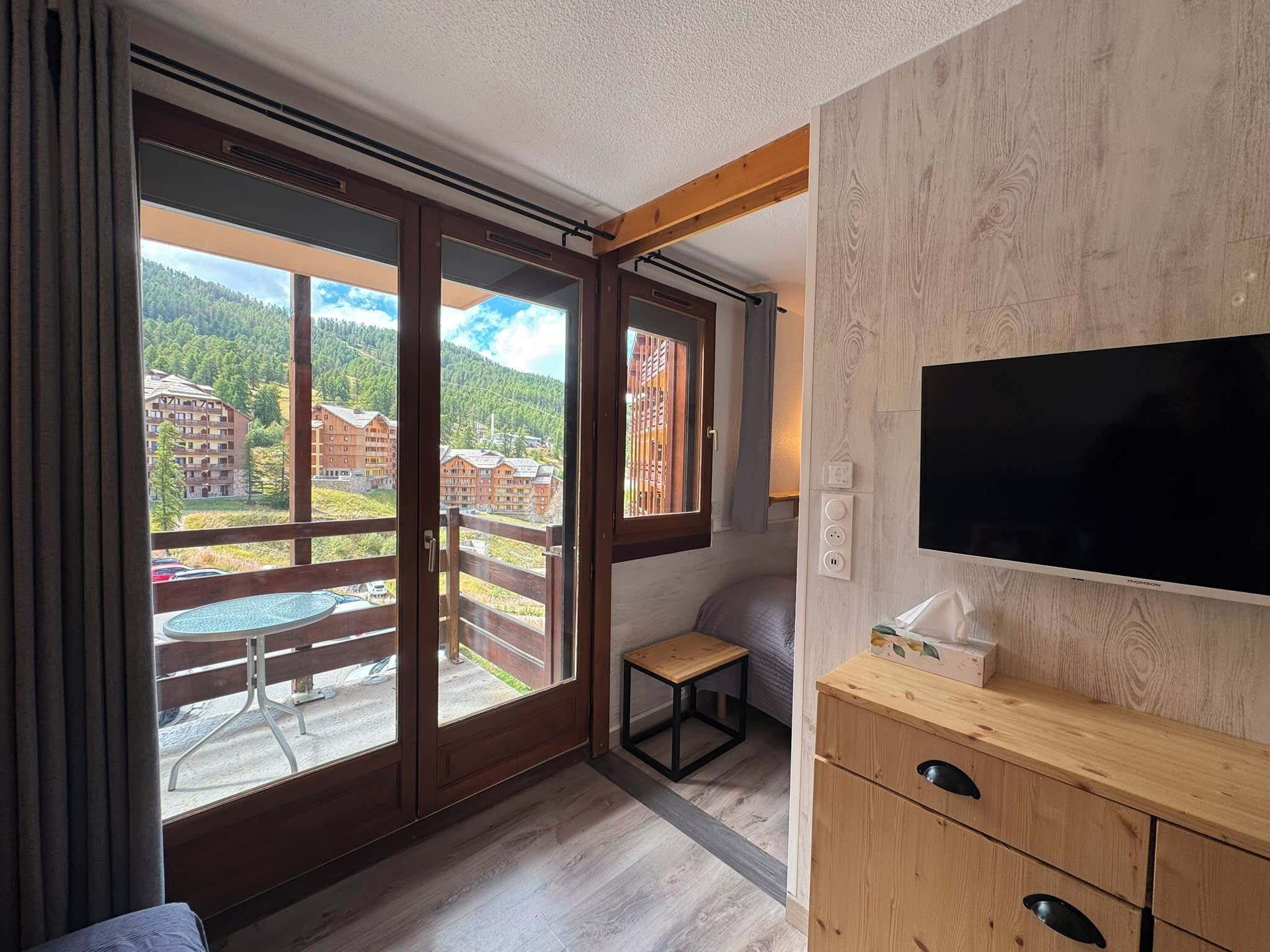 A hotel room with a balcony, a TV, a small table, and a wooden cabinet.