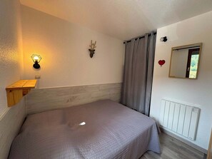 A bedroom with a bed, a wall-mounted light, a deer head decoration, a mirror, and a radiator. - Appartement cosy 4 pers à Risoul - Résidence Altaïr (Risoul)