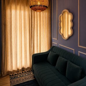Een kamer met een donkergroene bank, een kamerbreed tapijt met dessin en een decoratief wandobject.