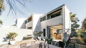 Una casa moderna con un patio, mobiliario exterior y vista al interior.