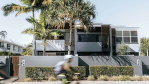 Un edificio moderno con techo plano, ventanas amplias y un árbol en primer plano.