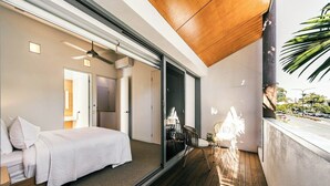 Un dormitorio moderno con cama, una mesita y una silla, además de un balcón con vistas a la calle.