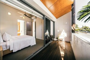 Ein modernes Schlafzimmer mit Bett, einem kleinen Tisch und einem Sessel, sowie einem Balkon mit Blick auf die Straße.