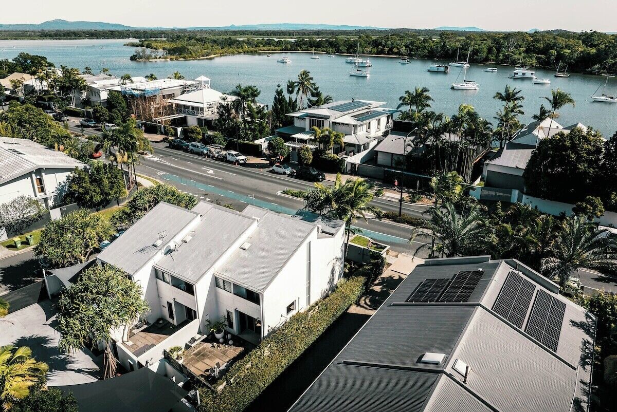 Un quartier résidentiel situé sur la côte, avec des maisons modernes, une marina remplie de bateaux et une vue dégagée sur l’eau.