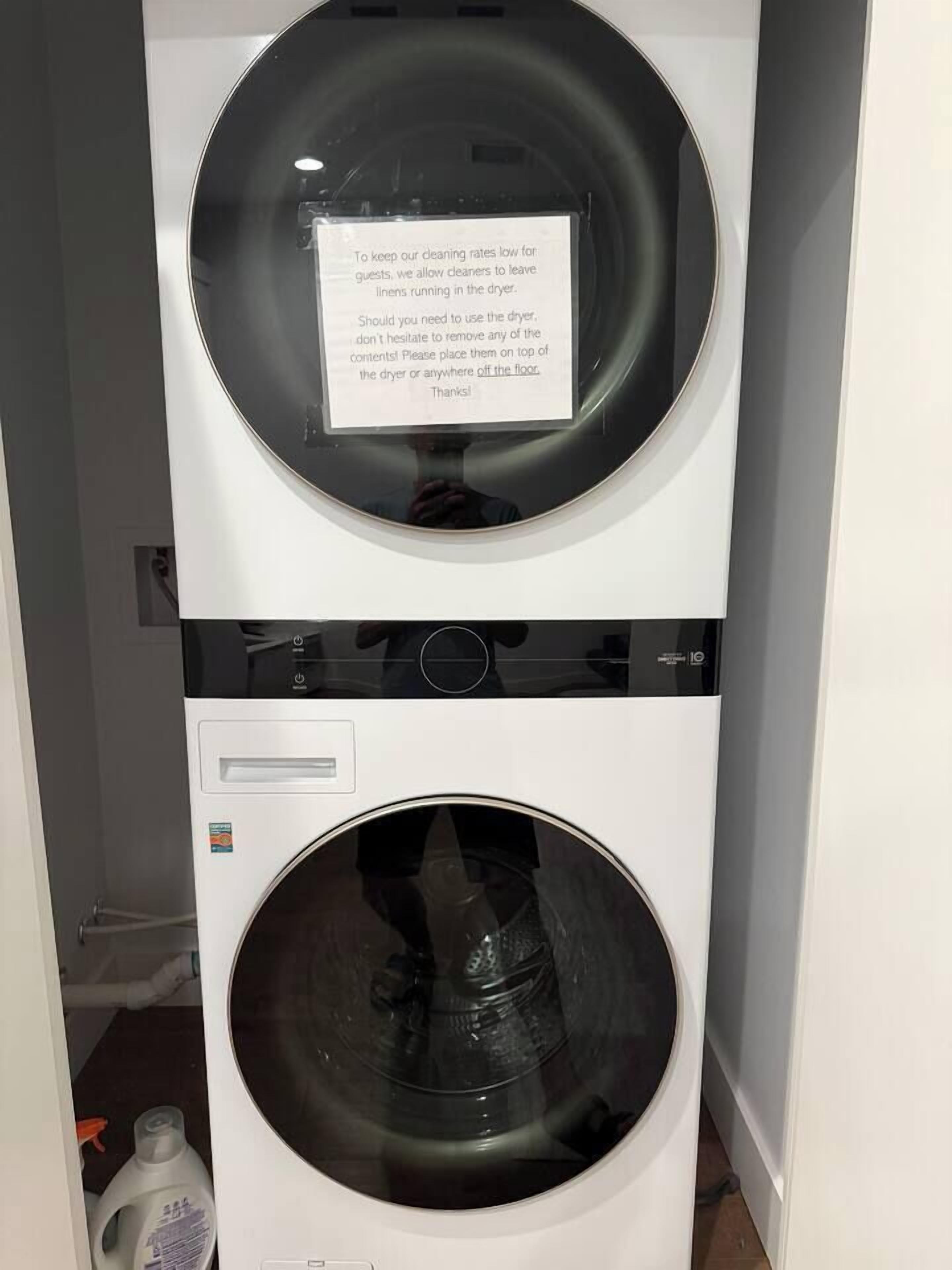 A stacked washer and dryer unit with a note advising guests to leave linens in the dryer to keep cleaning rates low.