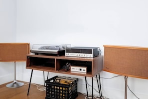A room with a wooden cabinet holding audio equipment, a black crate with items, and two large speakers. - New Modern Artist’s Studio - 2 units in 1 listing! (Oklahoma City)