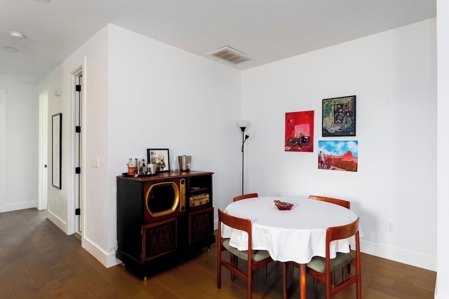 A dining area with a round table, chairs, a cabinet with a vintage radio, and wall art.