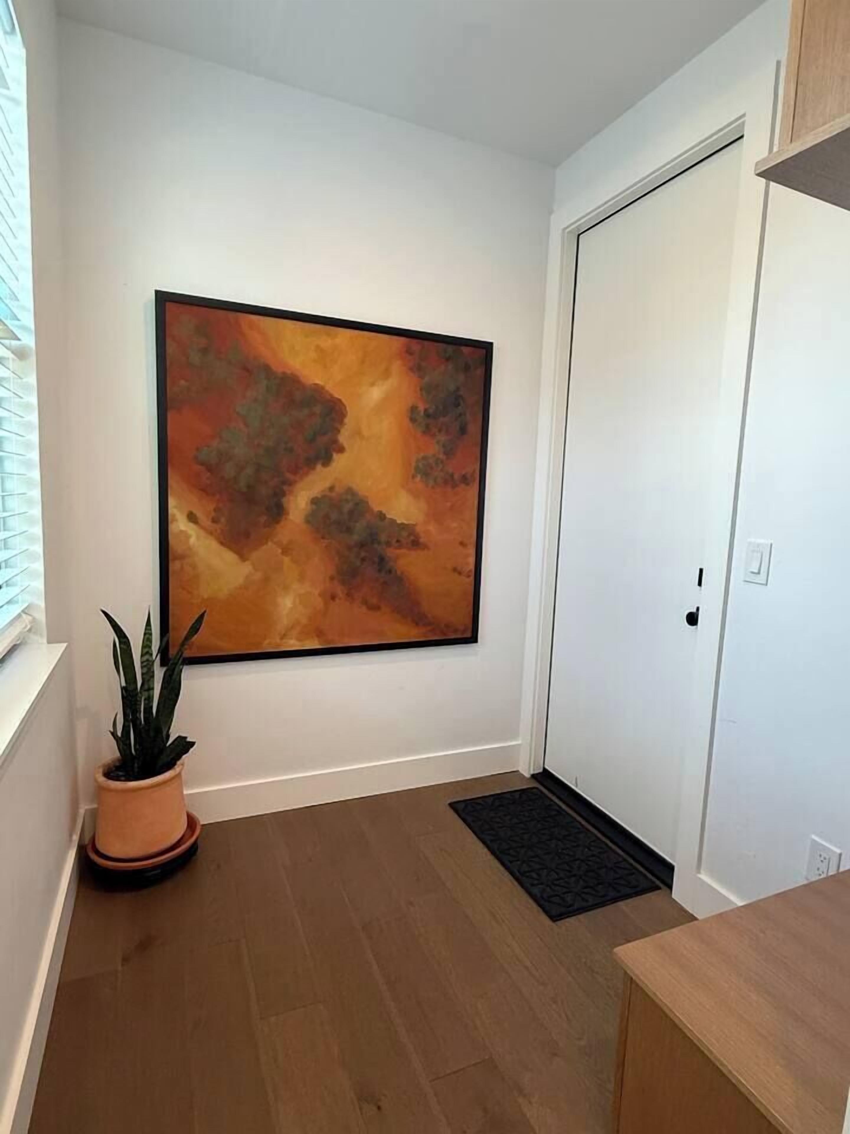 A hallway with a large abstract painting, a potted plant, a door, and a small rug.