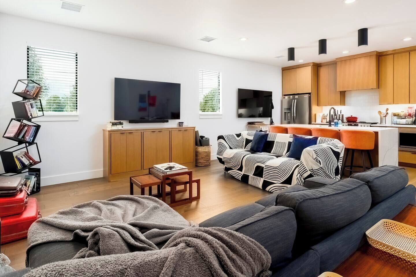 A modern living room with a sofa, a coffee table, and a TV. There is a kitchen area with wooden cabinets and a refrigerator.