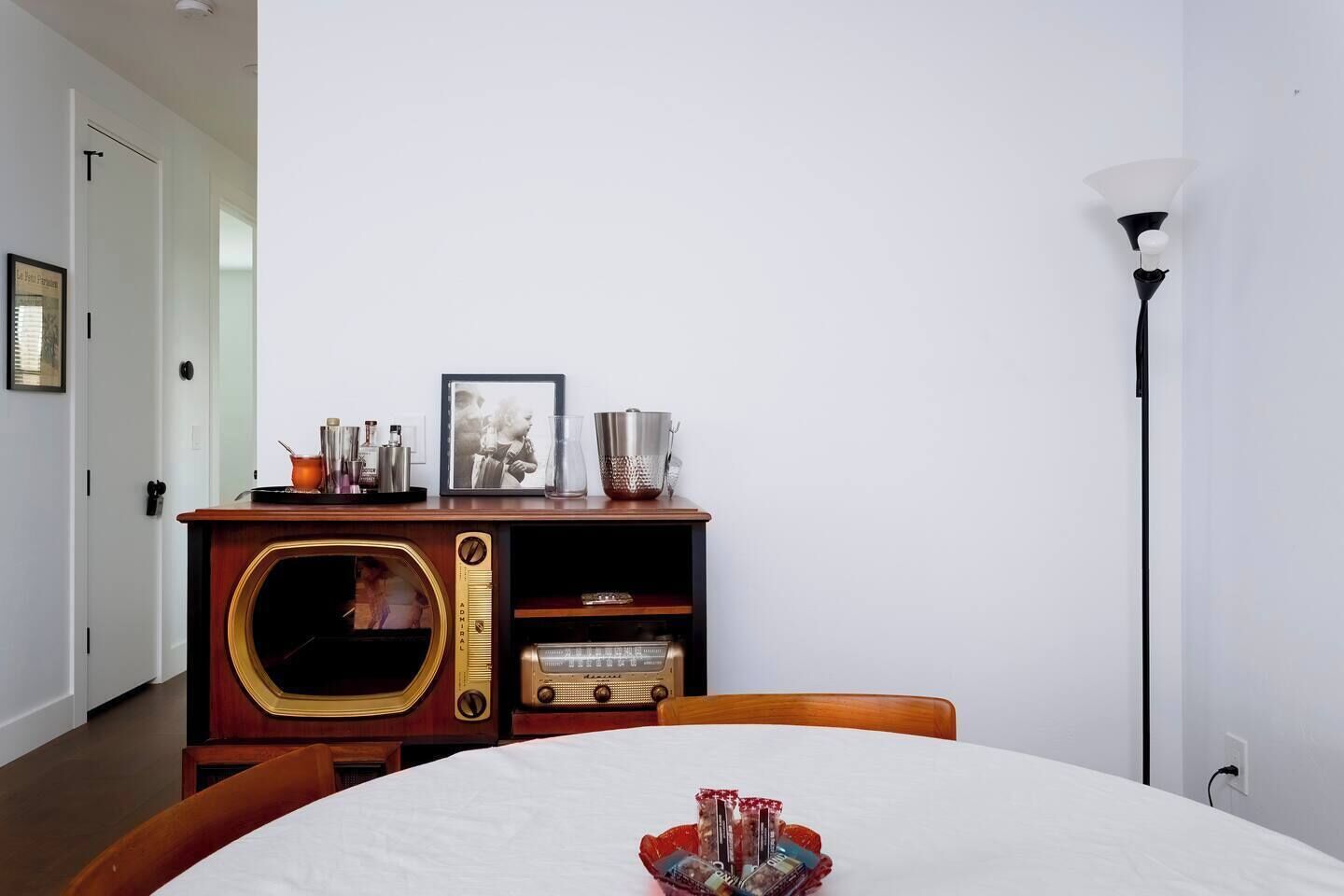 A room with a wooden cabinet, a framed picture, and a table with a white tablecloth.