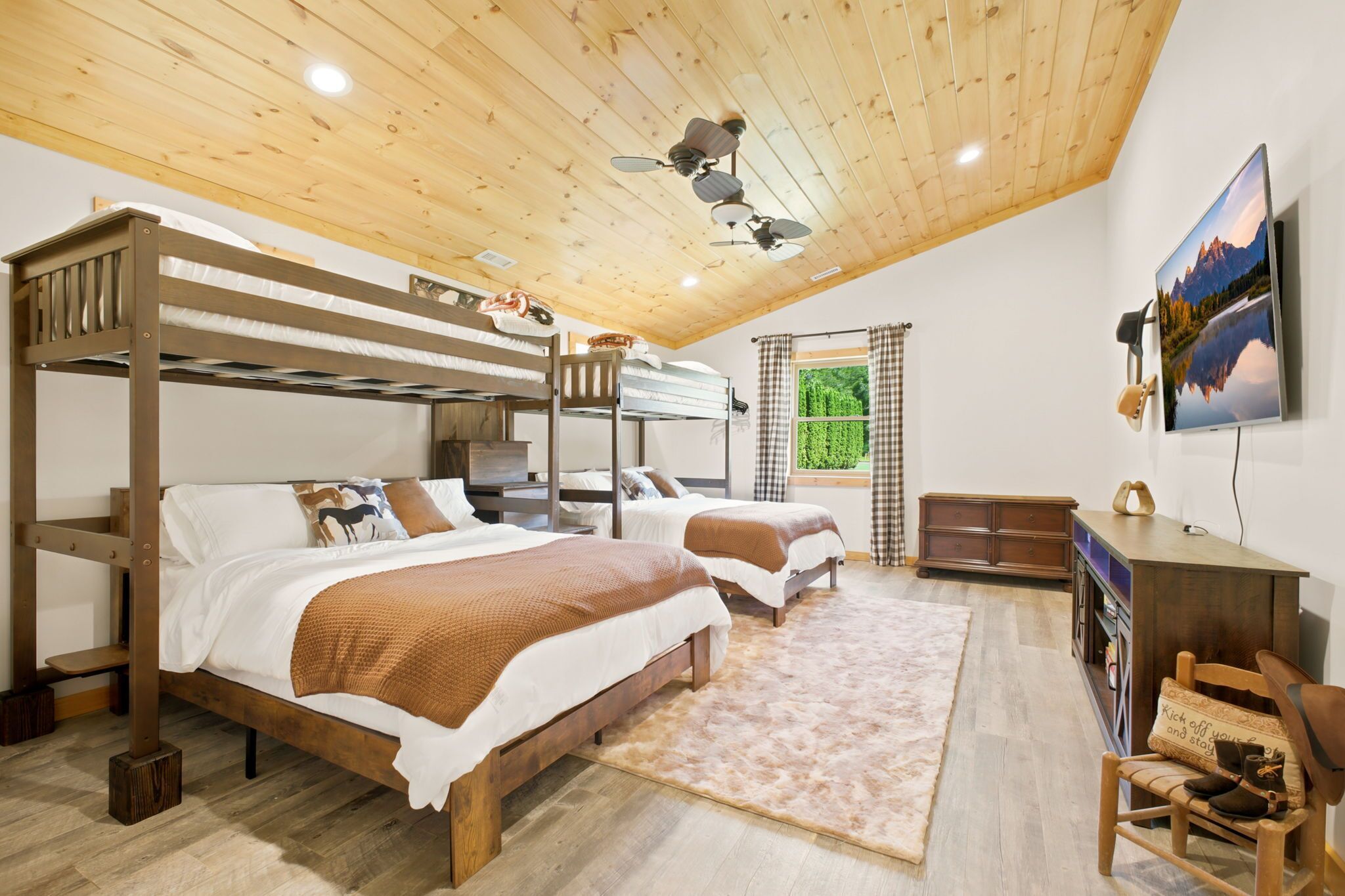 A room with bunk beds, a ceiling fan, a mounted TV, and a wooden desk.