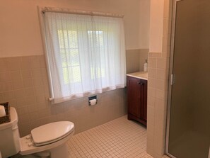 A bathroom with a toilet, a window with a curtain, a sink, and a cabinet.