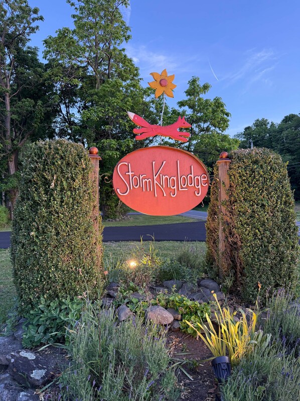 A sign for StormKing Lodge with a decorative flower and fox atop it, surrounded by greenery and a paved path.
