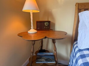Et natbord i træ med en lampe og en radio, en bog, og en seng med et blåt og hvidt ternet tæppe.