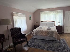 Un dormitorio con cama, una silla, una mesita de noche, una lámpara y una puerta.