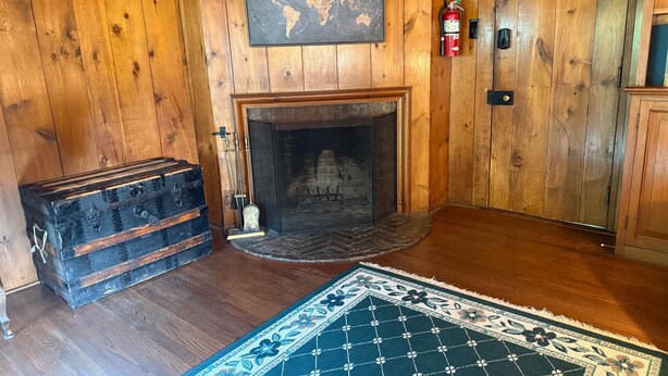 A wooden-paneled room with a fireplace, a world map, a fire extinguisher, and a vintage suitcase.