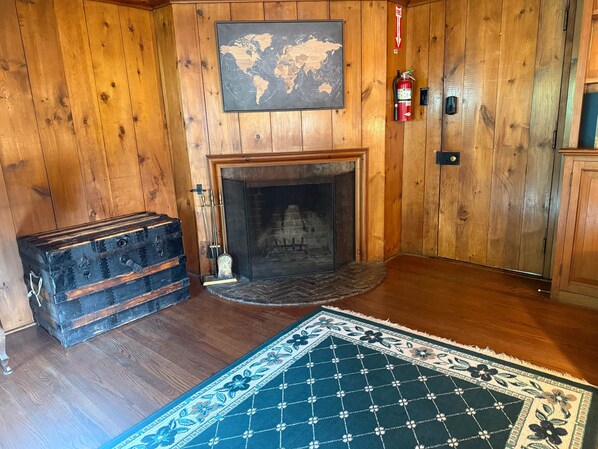 A wooden-paneled room with a fireplace, a world map, a fire extinguisher, and a vintage suitcase.