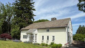 A two-story house with a front porch, a stone chimney, and a well-maintained lawn. - Pine Suite with Private Bath at Storm King Lodge (New Windsor)