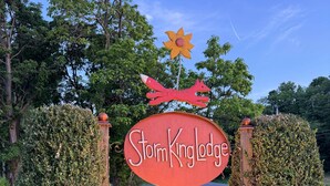 A sign for StormKing Lodge with a decorative flower and fox atop it, surrounded by greenery and a paved path. - Pine Suite with Private Bath at Storm King Lodge (New Windsor)