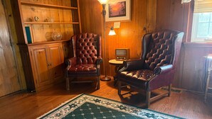 A room with wooden paneling, two leather armchairs, a small table with a lamp, and a rug.