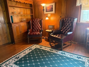 A room with wooden paneling, two leather armchairs, a small table with a lamp, and a rug.