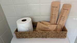 A bathroom with a toilet, a roll of toilet paper, and two brown paper bags labeled 'Shaving Kit' and 'Dental Kit'. - Pine Suite with Private Bath at Storm King Lodge (New Windsor)