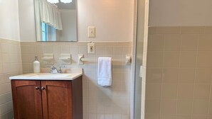 A bathroom with a wooden cabinet, a sink, a mirror, a towel rack, and a vent. - Pine Suite with Private Bath at Storm King Lodge (New Windsor)