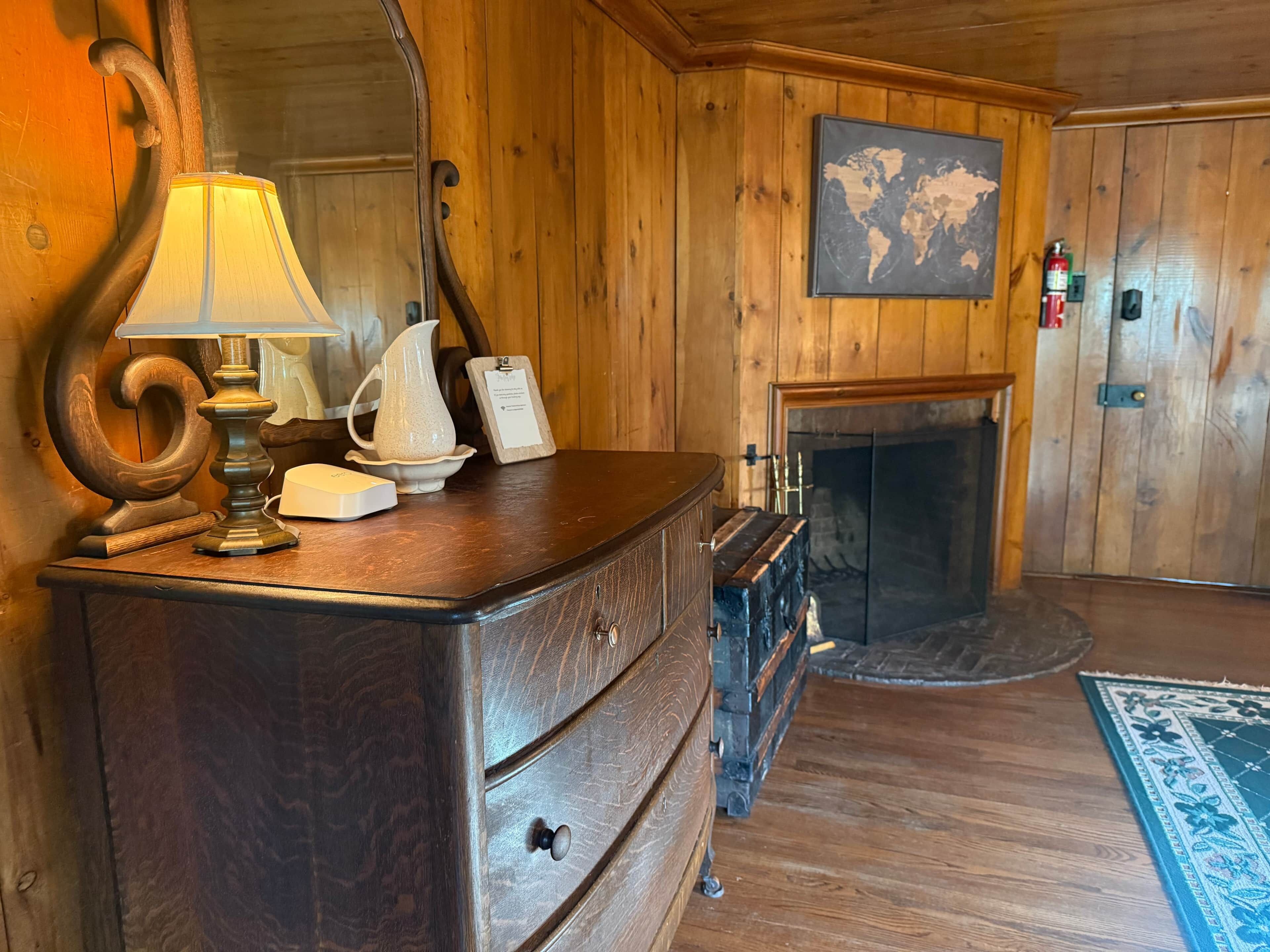 A wooden interior with a dresser, lamp, pitcher, and a world map on the wall.