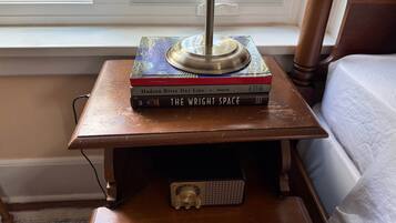 A wooden bedside table with a lamp, a stack of books, and a small electronic device.
