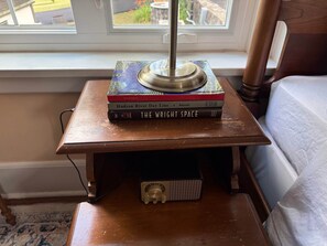 Et natbord i træ med en lampe, en stak bøger og en lille elektronisk enhed.