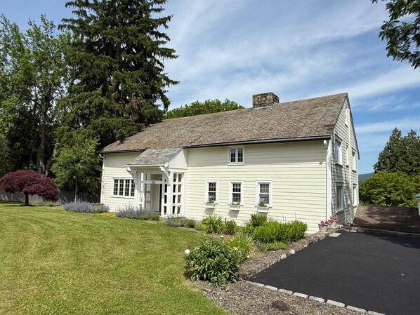 A two-story house with a front porch, a stone chimney, and a well-maintained lawn.