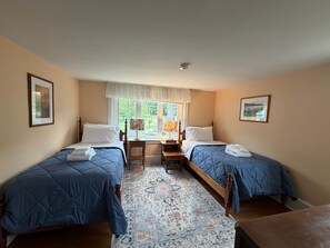 A room with two beds, a window with a view, a small table, and a rug.