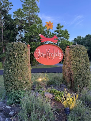 A sign for StormKing Lodge with a decorative flower and fox atop it, surrounded by greenery and a paved path.