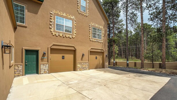 A two-story building with a garage entrance, a green door, and a clear driveway. - Ponderosa Glade! Hot Tub & Forest Views by USAFA (Monument)