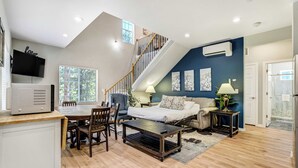 A modern living space with a dining area, a sofa, a bed, a staircase, and a TV. - Ponderosa Glade! Hot Tub & Forest Views by USAFA (Monument)